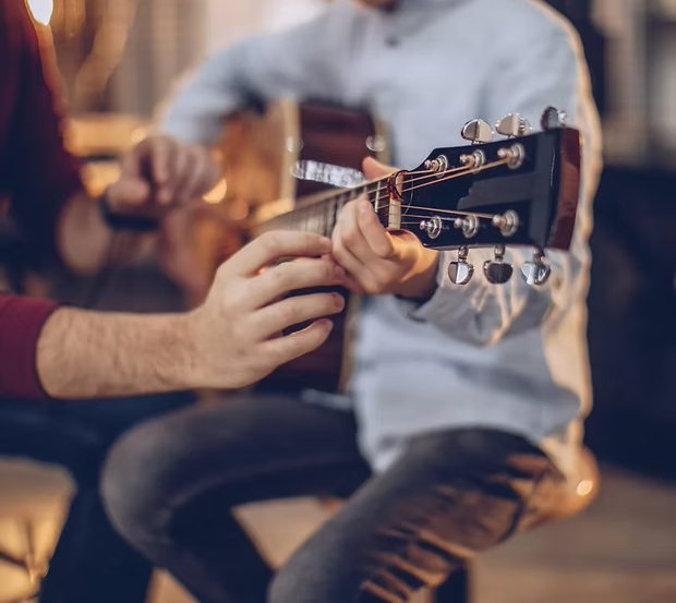 A guitar instructor teaching a student guitar chords